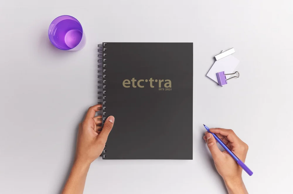 Ett svart spiralblock med Etceteras logotyp på i guld. Bilden är ett exempel på trycksaker